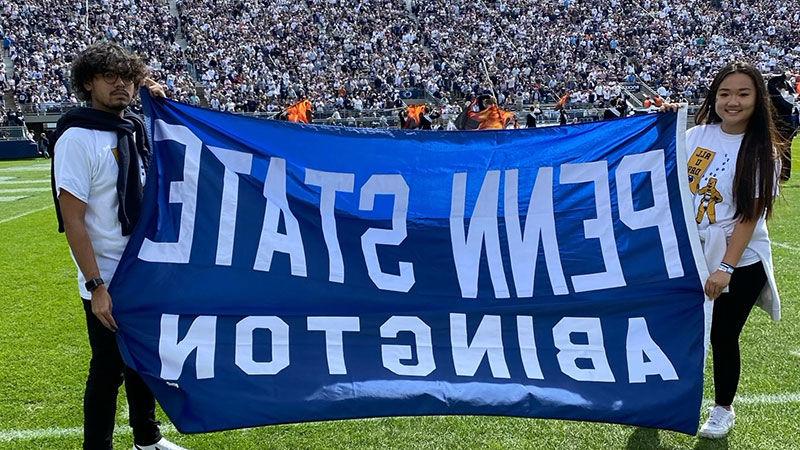 two students at Beaver Stadium with Penn State Abington banner